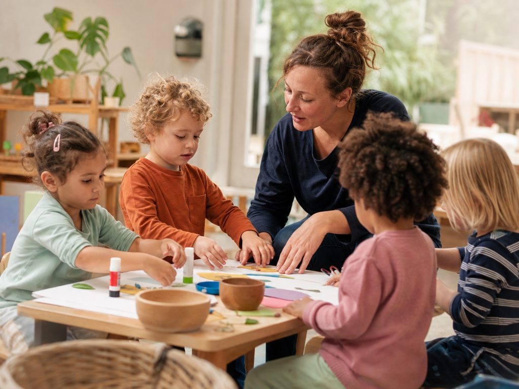 Eine Kindertagespflegeperson gestaltet mit Kindern am Tisch