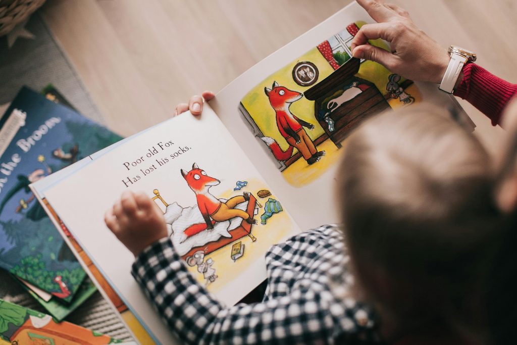 Eine Betreuungsperson liest mit einem Kind ein Bilderbuch